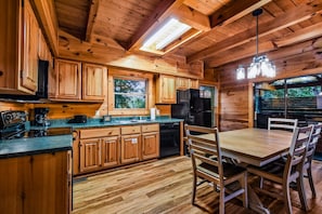 Interior de una cabaña de madera con comedor, cocina y un amplio ventanal.