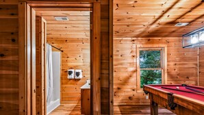 A wooden interior with a pool table, a window with a view, and a door leading to another room. - Silver Maple Summit 2 Bedroom Cabin (Gatlinburg)