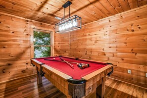 A pool table in a wooden room with a window and a hanging light fixture. - Silver Maple Summit 2 Bedroom Cabin (Gatlinburg)