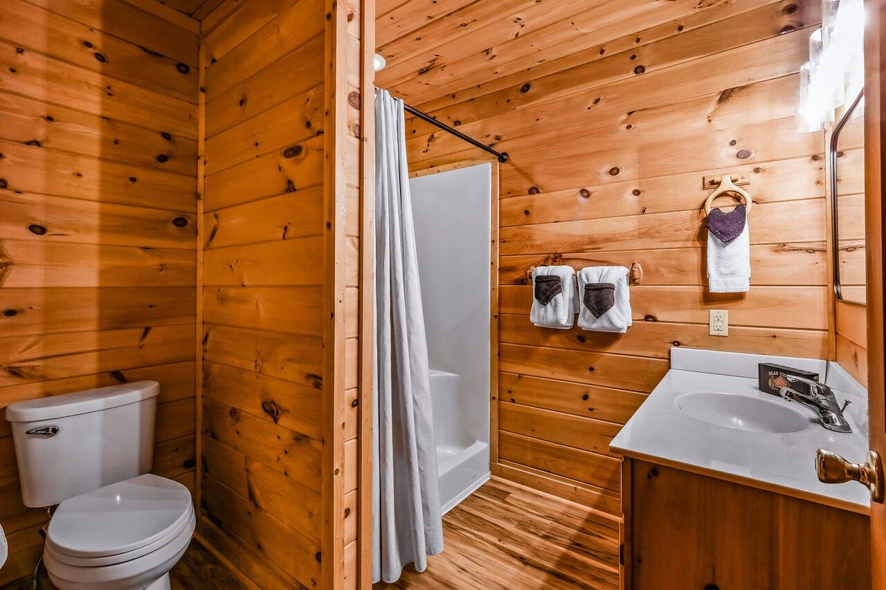 A wooden cabin bathroom with a toilet, shower, and sink.
