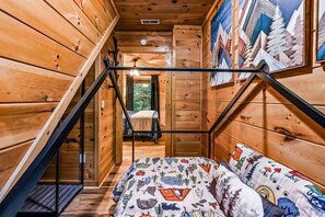 Ein Holzblockhaus-Interieur mit einem Bett, einer Treppe und einem Gemälde von Bergen.