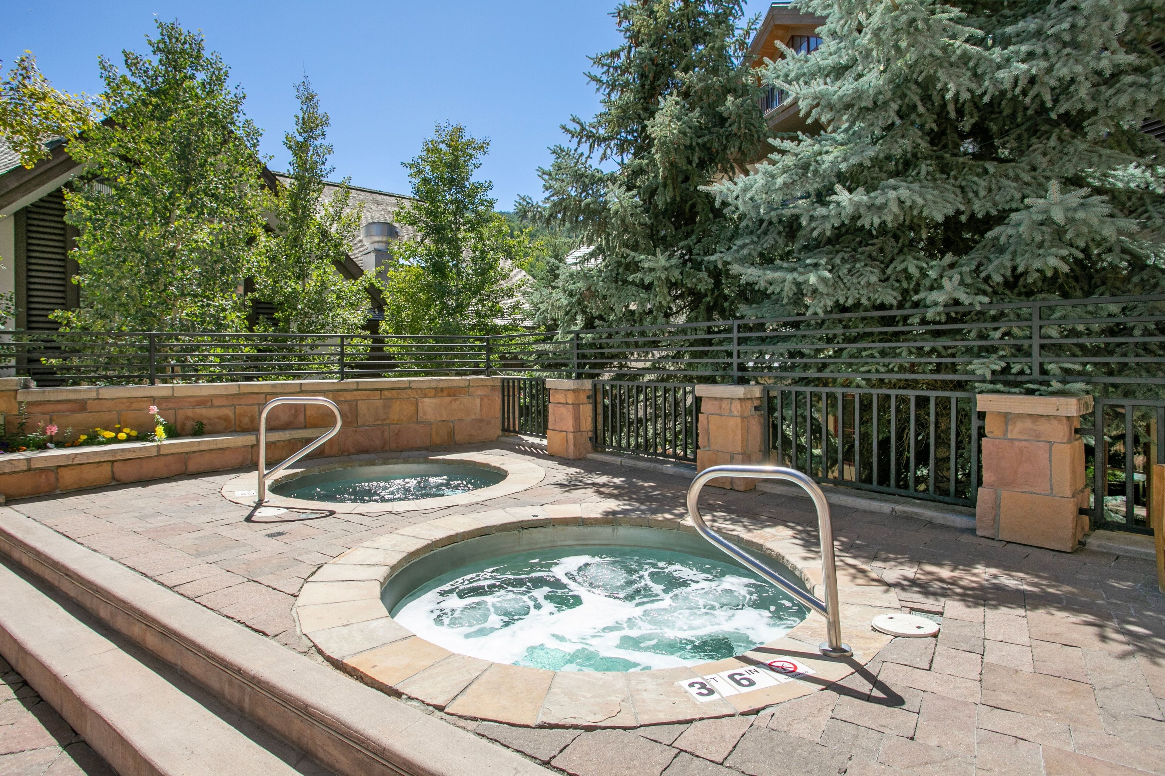 Ein Poolbereich mit zwei Whirlpools, Steintreppen und einem Metallzaun.