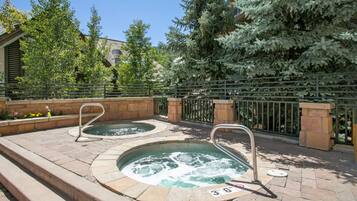 A pool area with two hot tubs, stone steps, and a metal fence.