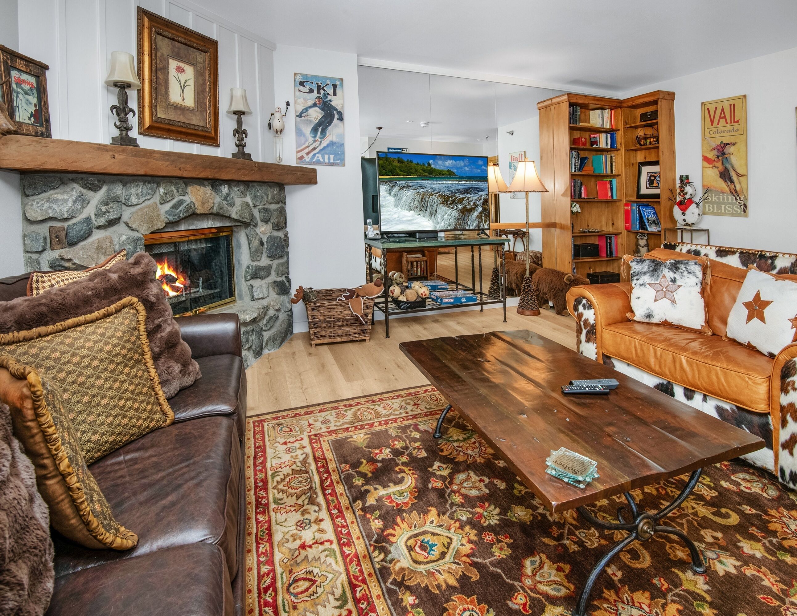 Ein gemütliches Wohnzimmer mit Kamin aus Stein, Ledersofa, Holztisch und Bücherregal.