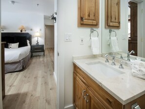 Hotelkamer met een bed, nachtkastje met lamp, houten kasten, een grote spiegel en een badkamer met wastafel en handdoekhouder.