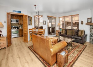 Ein geräumiger Wohnbereich mit einer Ledersofa, einem Esstisch mit Stühlen, einer Küche mit Holzschränken und großen Fenstern mit Jalousien.