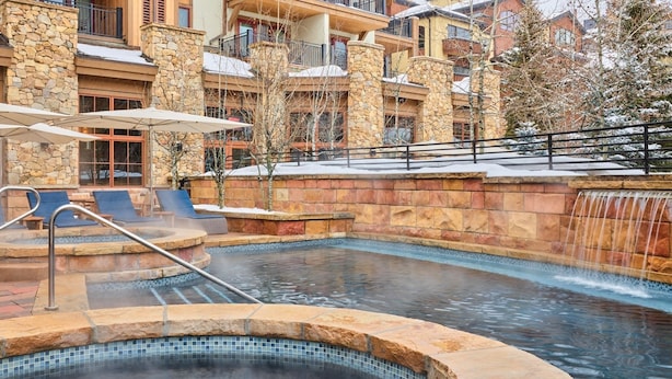 A pool area with stone walls, lounge chairs, and a waterfall feature. - Village Inn Plaza 218 2 Bedroom Condo (Vail)