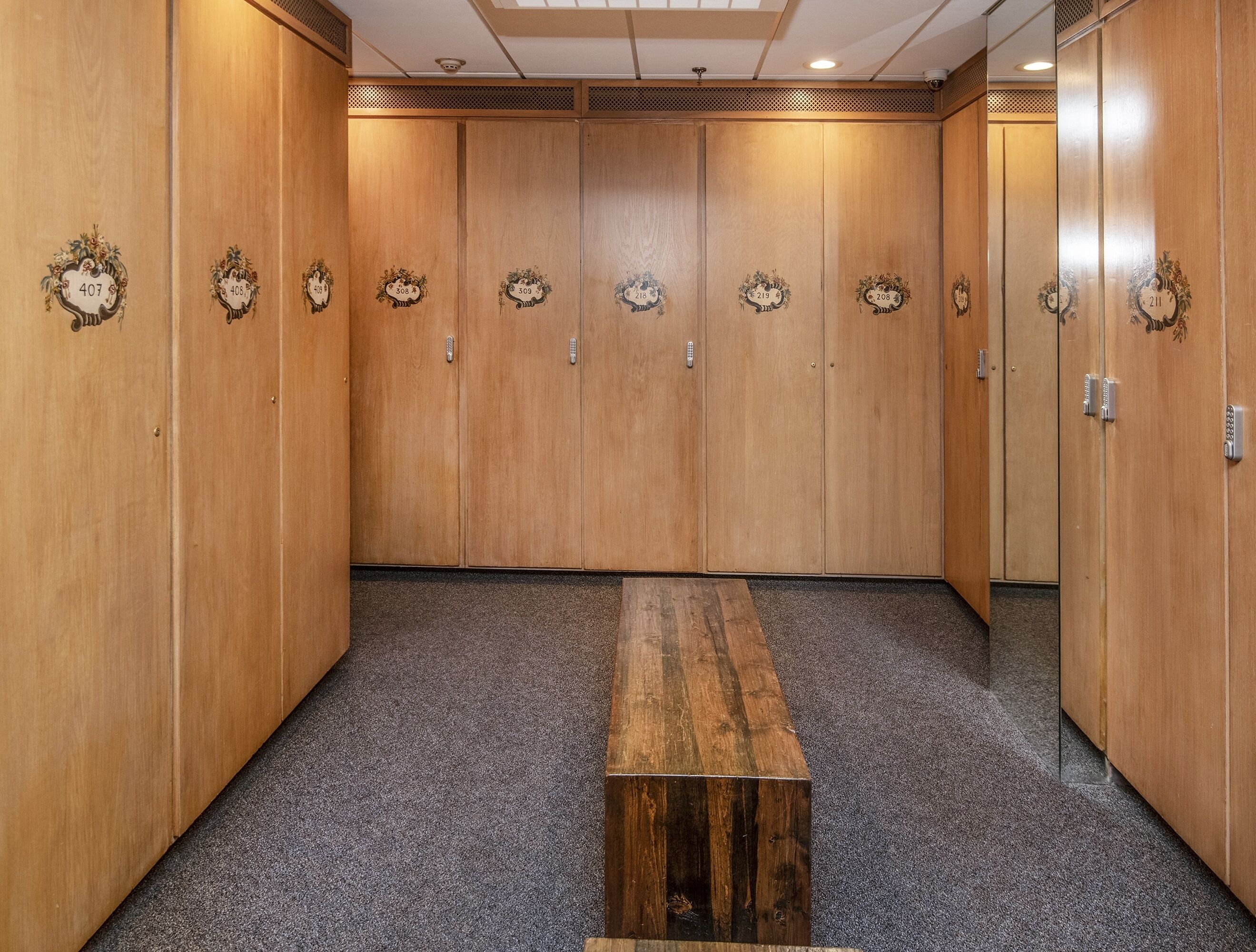 A row of wooden lockers with numbers, a bench, and a carpeted floor.