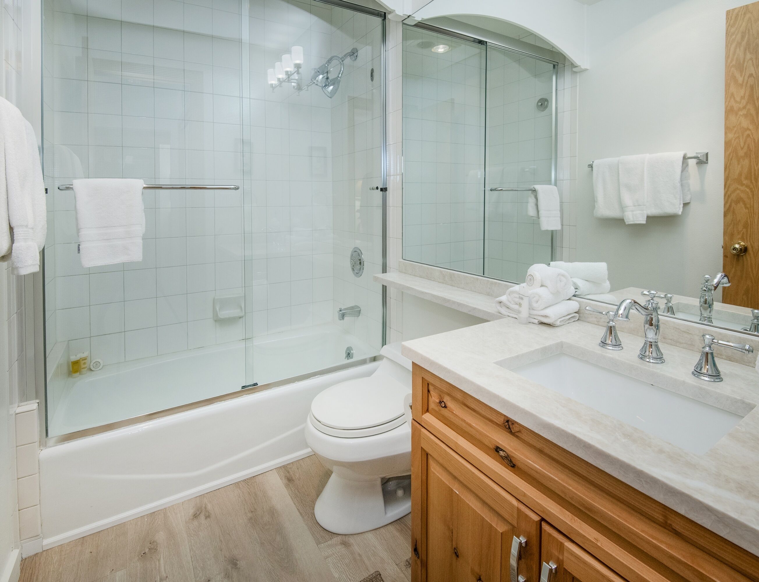 A modern bathroom with a glass-enclosed shower, a white toilet, a vanity with a mirror, and a sink with chrome fixtures.