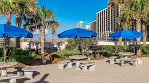 Outdoor seating with blue umbrellas, stone tables, and a brick patio. - Phoenix East 804 2 Bedroom Condo (Orange Beach)
