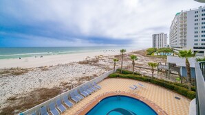 A beach view from a balcony with a swimming pool, lounge chairs, and a high-rise building in the background. - Phoenix Ix 302 2 Bedroom Condo (Orange Beach)