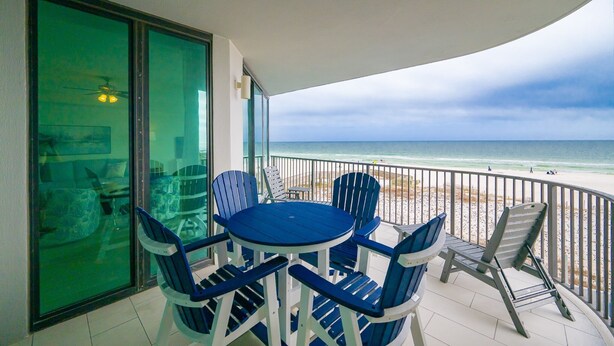 A balcony with a table and chairs, a glass door, and a view of the beach. - Phoenix Ix 302 2 Bedroom Condo (Orange Beach)