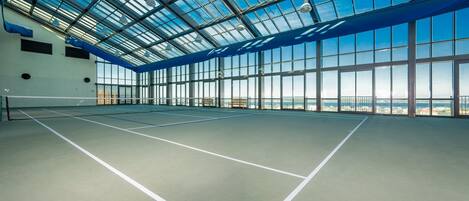 Una cancha de tenis interior con techo de vidrio y vistas a la ciudad.