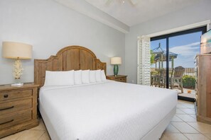 A hotel room with a large bed, wooden headboard, two bedside tables with lamps, a view of a balcony with outdoor furniture. - Phoenix V 013 2 Bedroom Condo (Orange Beach)