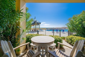 Eine Terrasse mit einem runden Tisch und Stühlen, einem Pavillon und Blick auf Pool und Strand.
