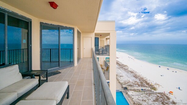 A balcony with a view of the beach, a pool, and a seating area. - Phoenix X 1504 3 Bedroom Condo (Orange Beach)