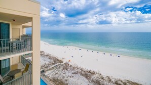 A beachfront hotel with balconies, a pool, and a sandy beach with umbrellas. - Phoenix X 1504 3 Bedroom Condo (Orange Beach)