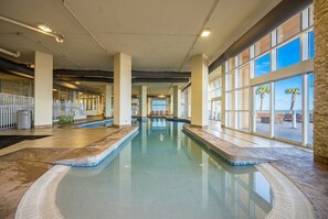 An indoor swimming pool with clear glass walls, a tiled floor, and a view of palm trees outside. - Phoenix Gulf Shores 1901 4 Bedroom Condo (Gulf Shores)