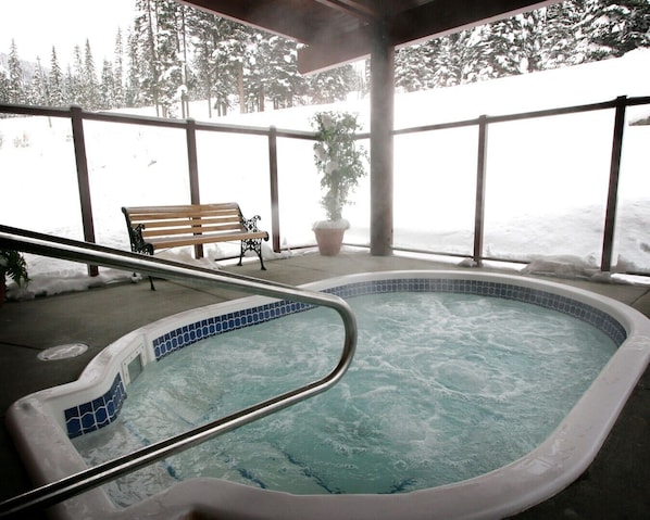 Un jacuzzi con borde de azulejos, un banco de madera y una planta en maceta.