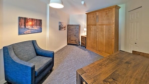 A room with a blue armchair, a wooden table, a cabinet, and a painting on the wall. - Cahilty #205 Hotel Room (Sun Peaks)