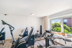 A gym with exercise equipment, a window with a view of greenery, and a white ceiling.