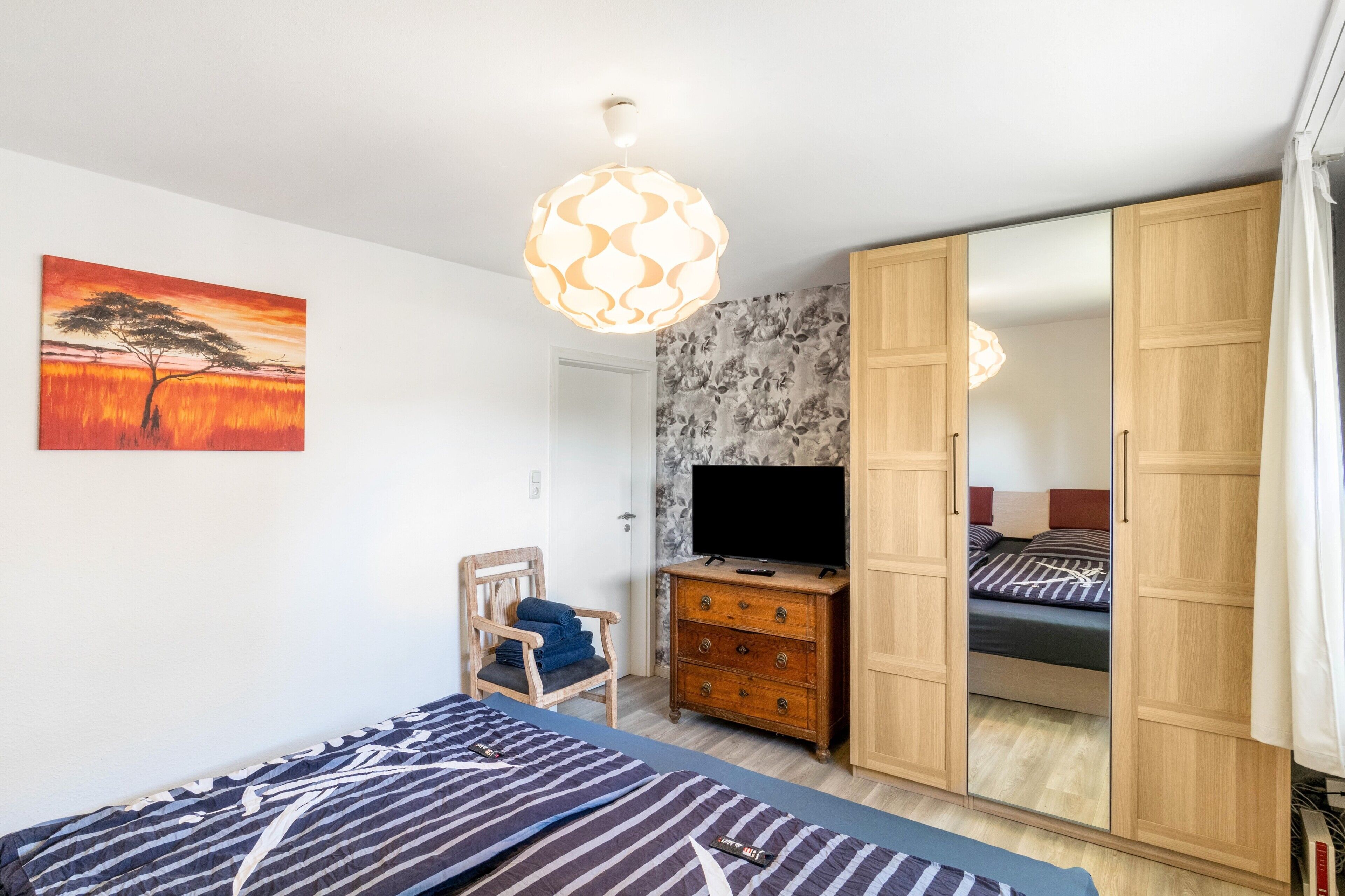 Ein Schlafzimmer mit Bett, Sessel, Kommode, Fernseher und Kleiderschrank.
