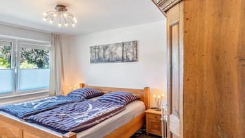 A bedroom with a wooden bed, a nightstand, a wall-mounted light fixture, and a window with curtains.