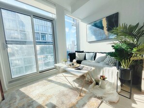 A modern living room with large windows, a sofa, a coffee table, and a potted plant. - Filmores Hotel (Toronto)