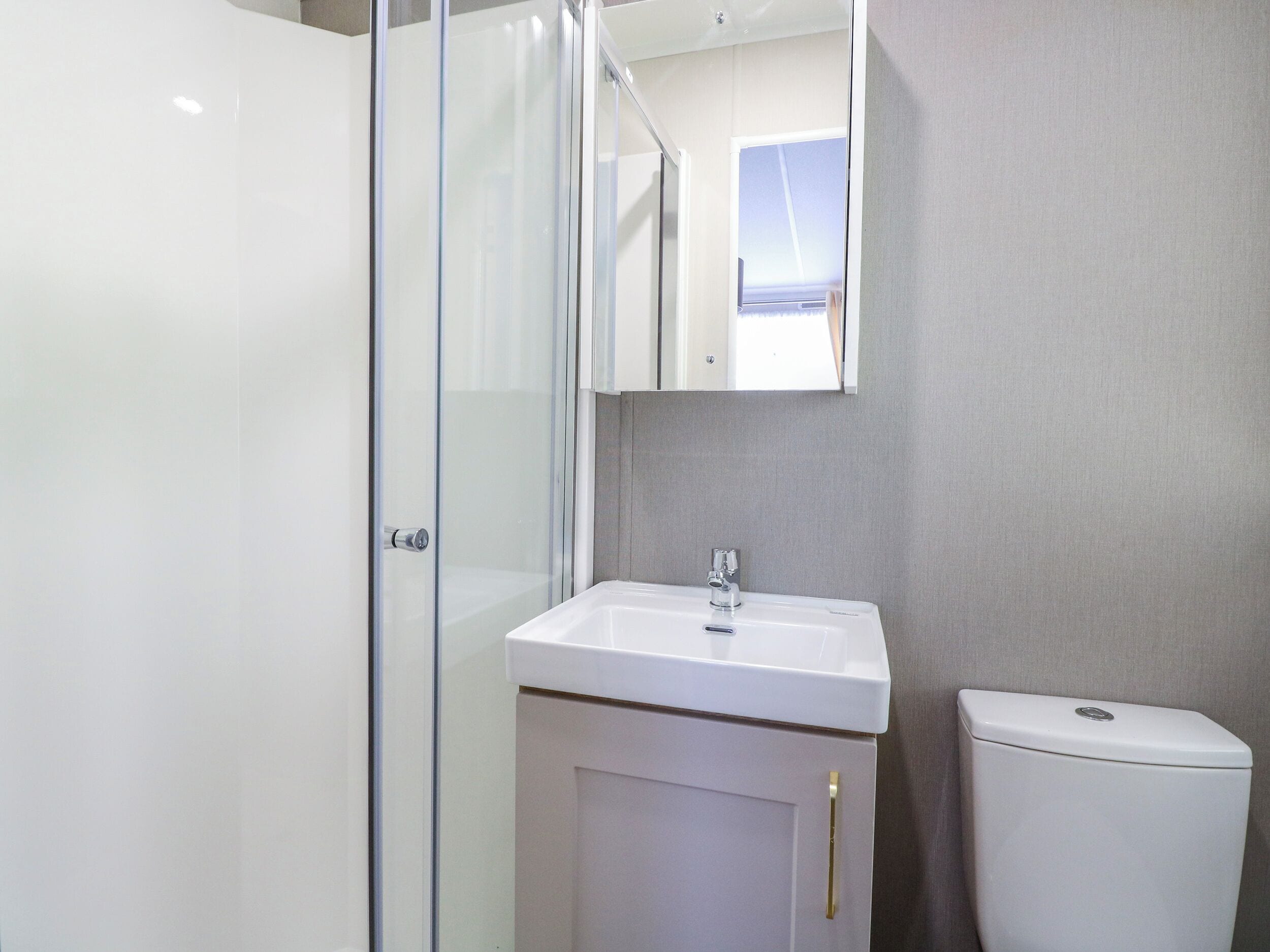 A bathroom with a glass shower enclosure, a white sink, and a toilet.