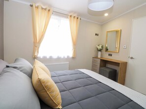 A bedroom with a bed, a bedside table, a mirror, and a window with curtains. - The Honey Pot Retreat (Great Yarmouth)