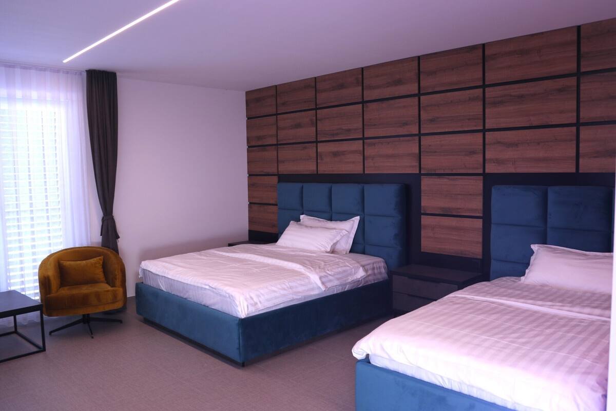 Habitación de hotel con dos camas, un escritorio, una silla y un ventanal con cortinas.