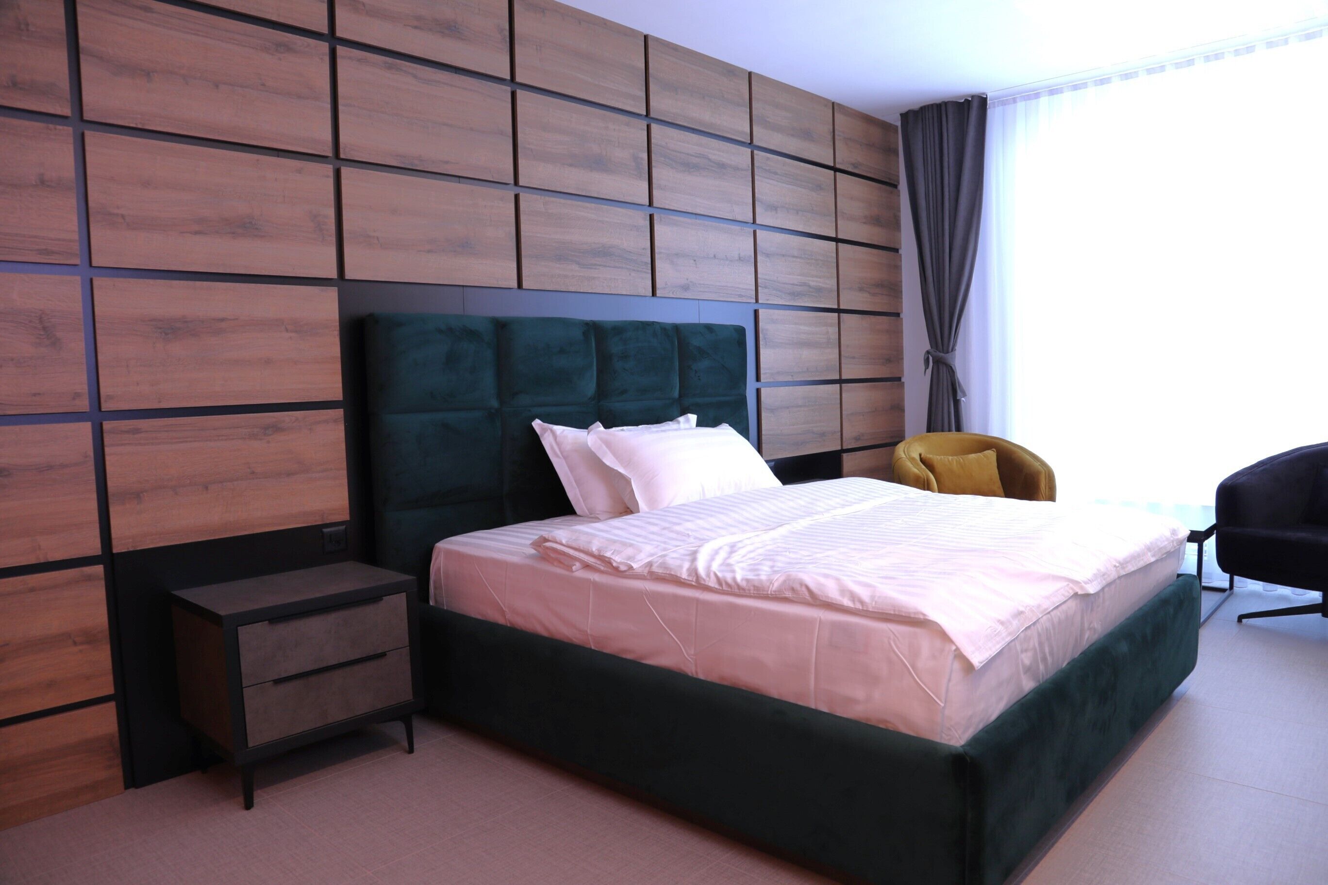 Ein modernes Hotelzimmer mit einem großen Bett, einem Nachttisch, einem Sessel und einer Wand aus Holzpaneelen.