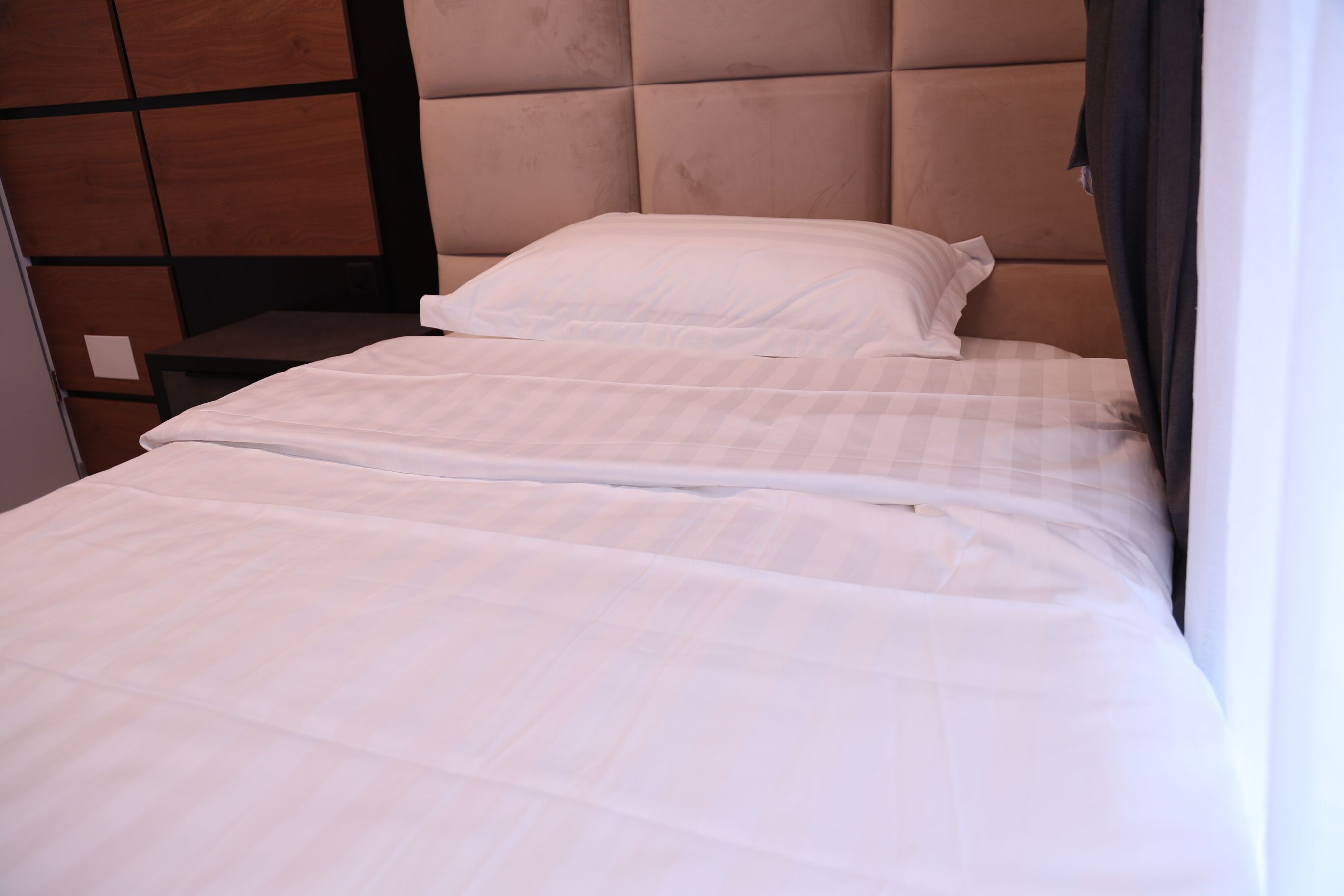 Una cama bien hecha con cabecera, una mesita de noche y una pared con paneles de madera.