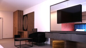 A modern room with a flat-screen TV, a black chair, a small table, and a wooden ottoman.