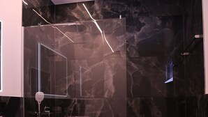 A modern bathroom with a marble wall, a glass shower enclosure, and a white sink.