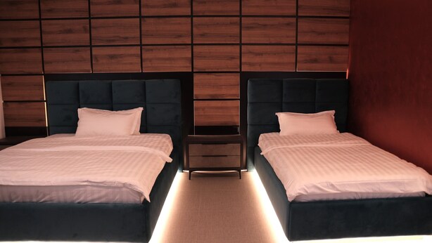 A hotel room with two beds, a nightstand, and a wooden panel wall.