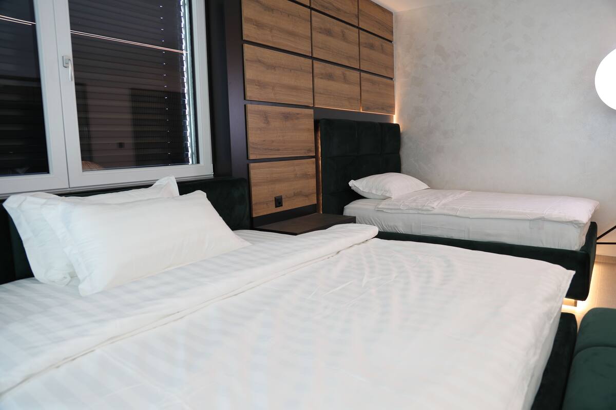 Un dormitorio con dos camas, una ventana con persianas y una lámpara fijada a la pared.