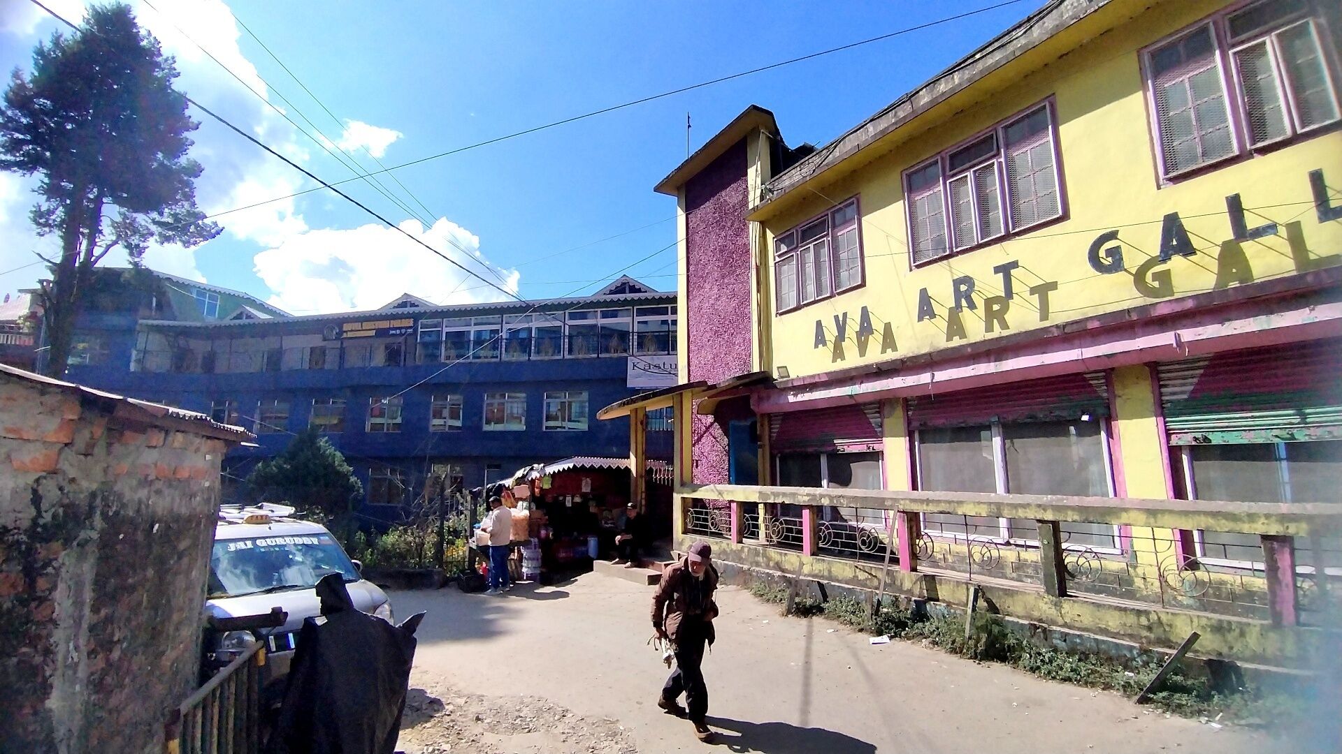 A street with a yellow building labeled 'AVA ART GALL,' a parked car, and a person walking.