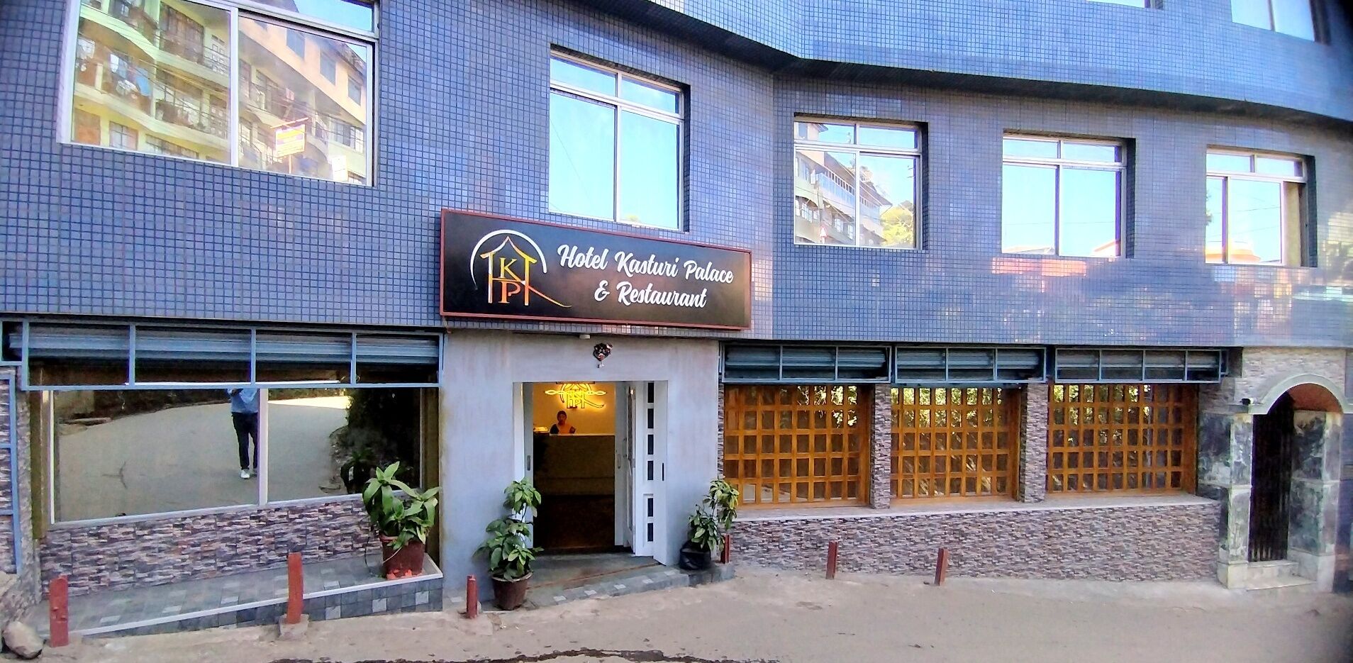 Un hotel con fachada de azulejos, un cartel que dice 'Hotel Kasturi Palace & Restaurant' y una entrada protegida por una reja.