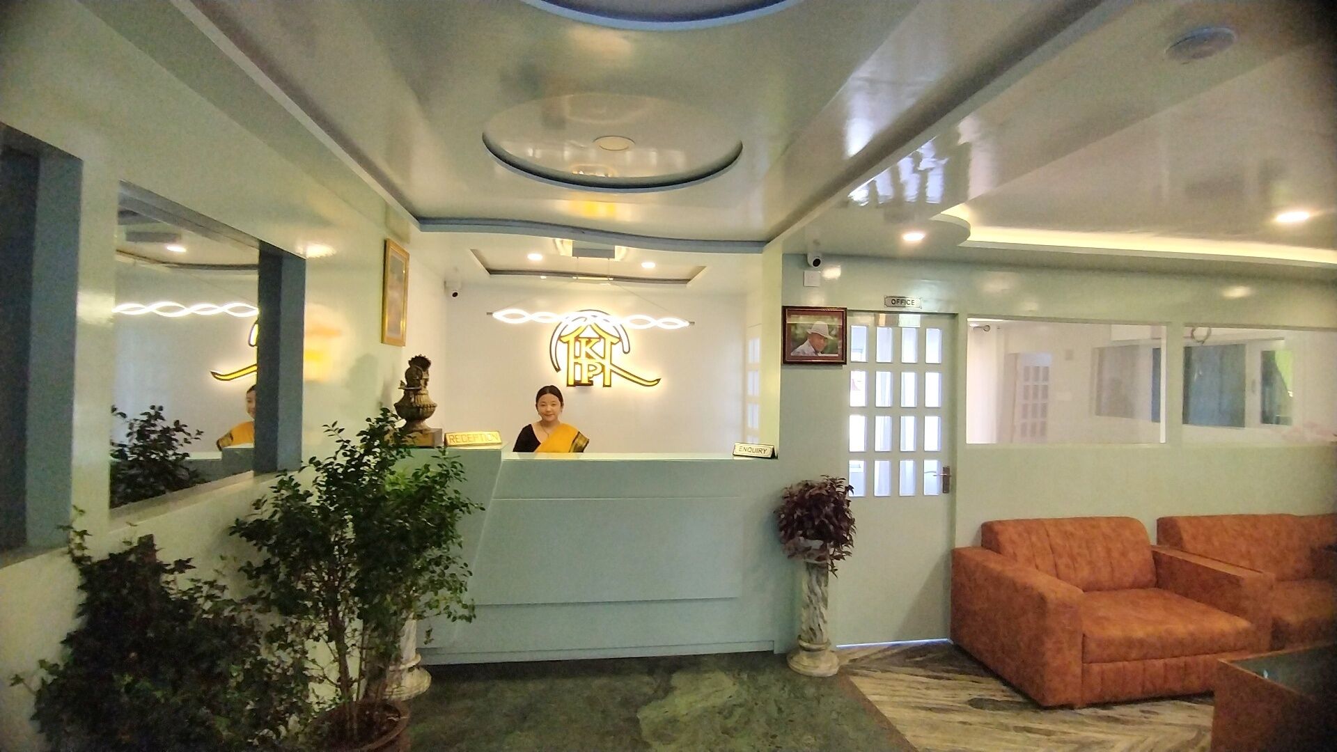 Un mostrador de recepción con una recepcionista, una zona de espera y un área de estar con dos sofás.