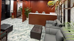 A reception area with a marble floor, wooden reception desk, grey sofa, and potted plants. - A ONE RESIDENCY (Gurugram)