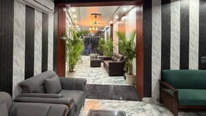 A hotel lobby with a marble floor, leather sofas, a coffee table, and potted plants. - A ONE RESIDENCY (Gurugram)