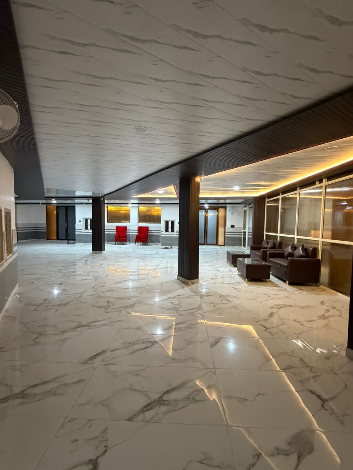 A spacious lobby with marble flooring, red chairs, sofas, and a modern ceiling design.