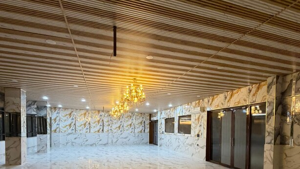 A spacious lobby with a polished marble floor, a wooden ceiling with a linear pattern, and a chandelier. - A ONE RESIDENCY (Gurugram)