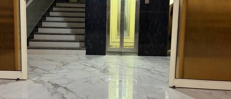 A marble-floored lobby with a staircase, a potted plant, and a double door elevator.