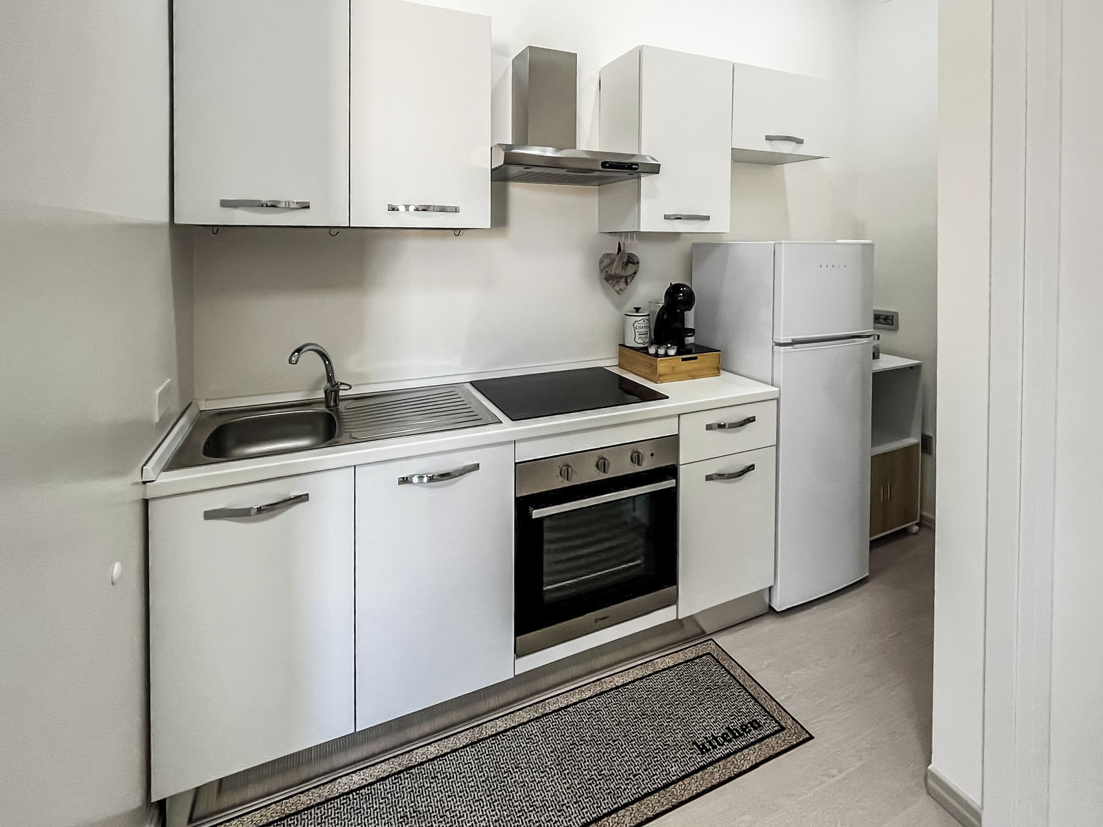 Eine kleine Küche mit weißen Schränken, einem Backofen, einer Spüle und einem Kühlschrank.