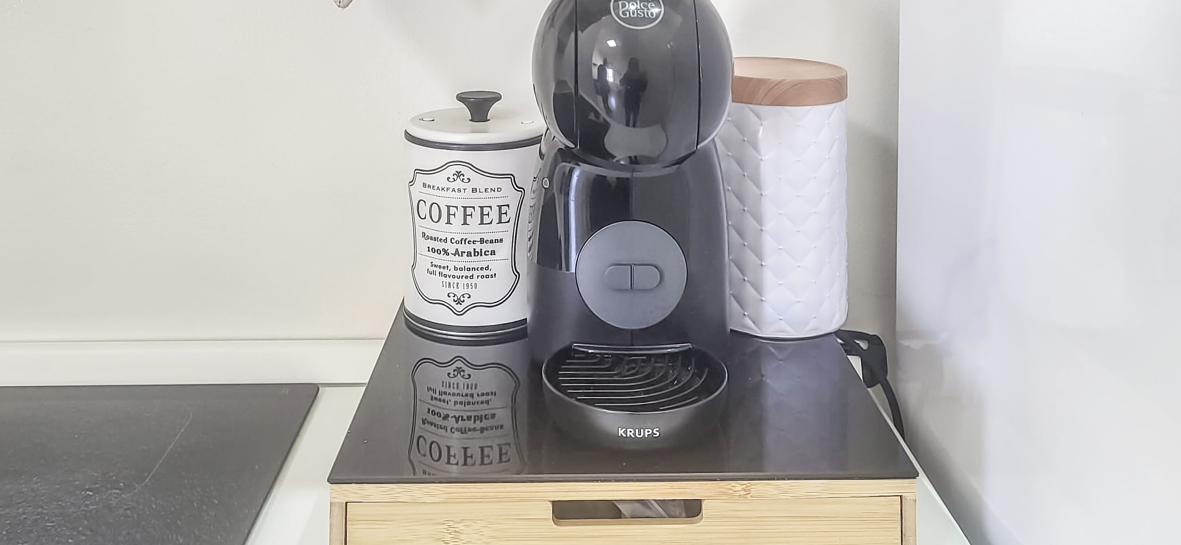 Une machine à café, un récipient à café et un porte-essuie-tout, le tout posé sur une table en bois.