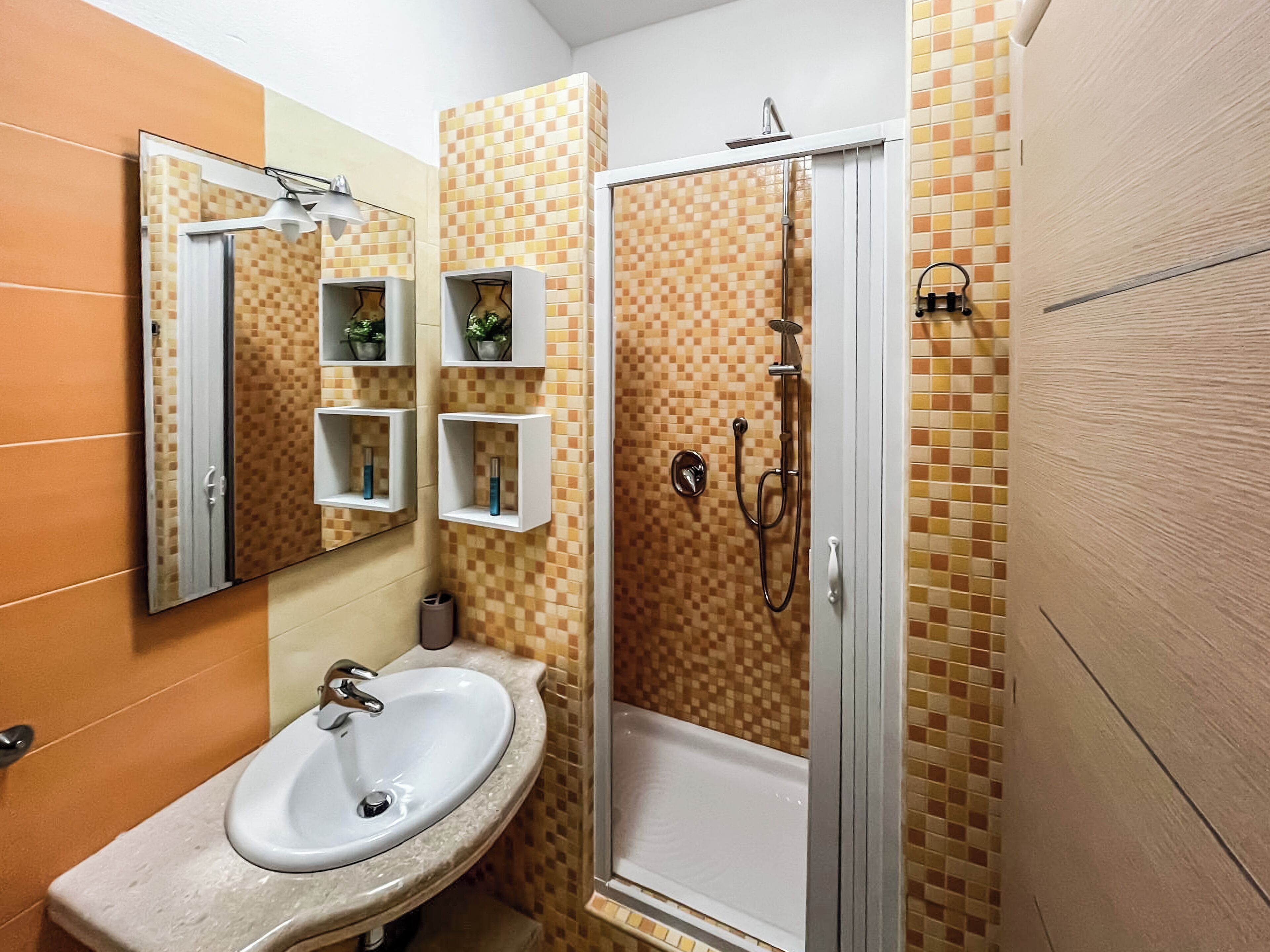 Ein Badezimmer mit Waschbecken, Spiegel, Ablagen für Toilettenartikel und einer Dusche.