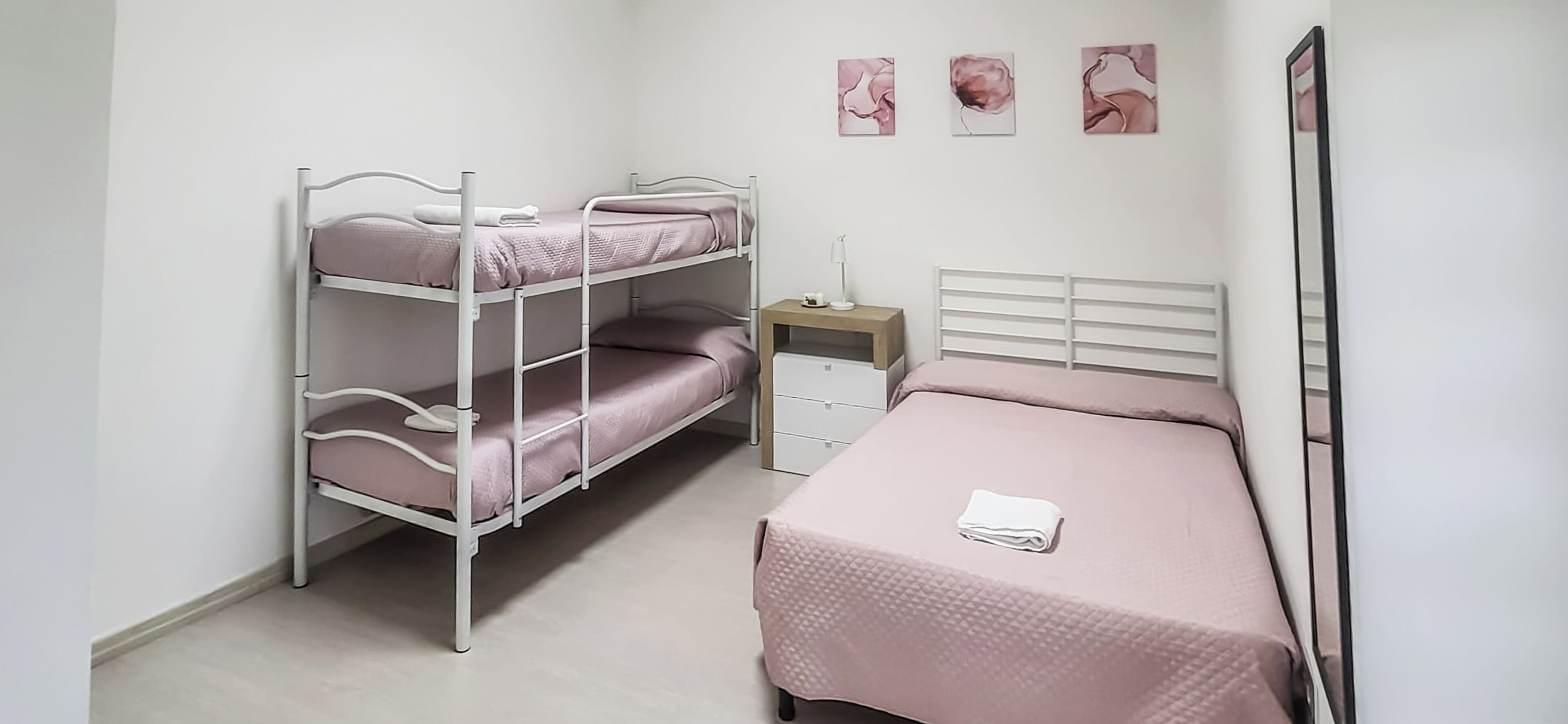 Dormitorio con literas, una cama individual, una mesita de noche y tres cuadros colgados en la pared.