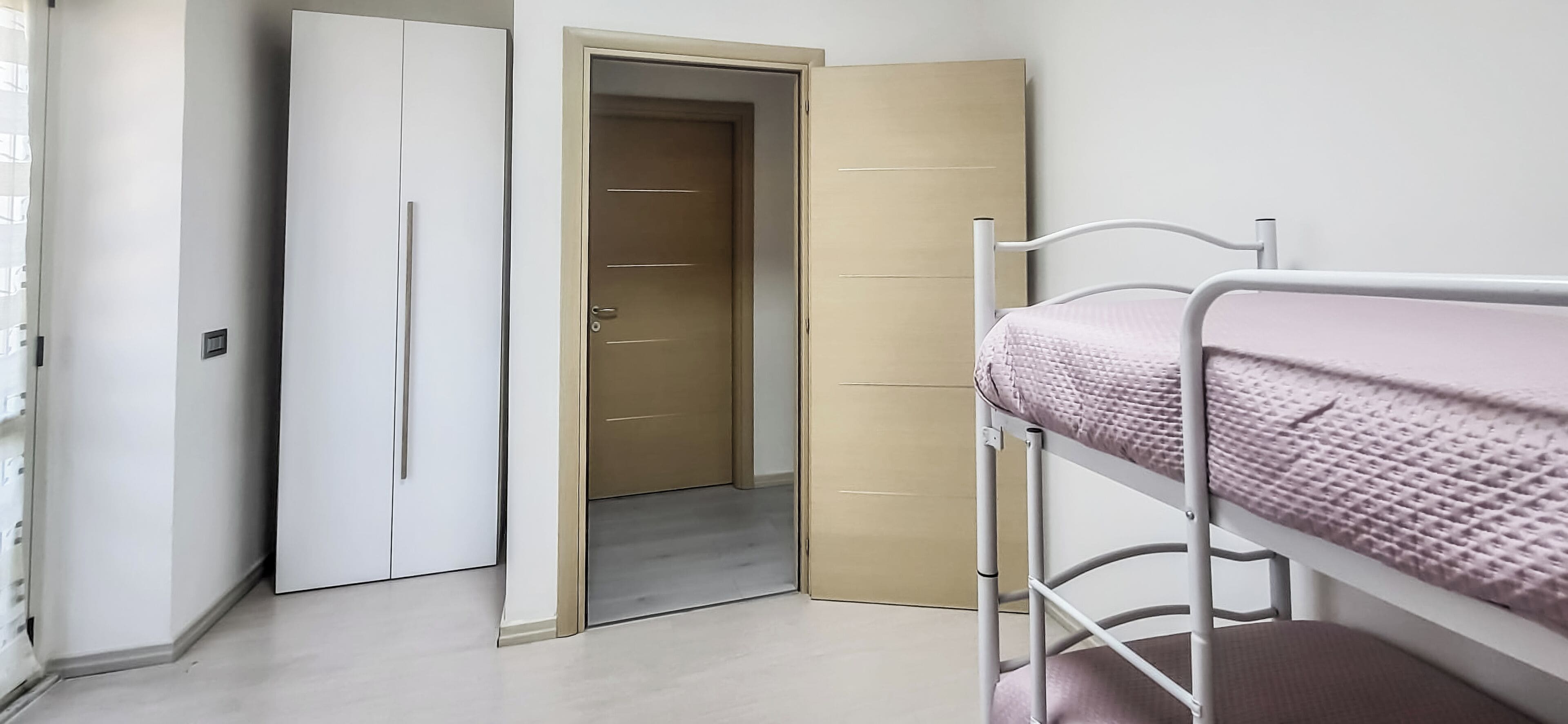 A room with a bunk bed, a wardrobe, and a door leading to another room.